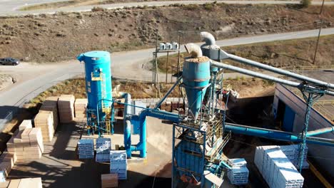 stellar-pan-zoom-drone-shot-of-a-blue-Sawmill-Processing-Plant-with-cars-and-bundles-of-boards-in-the-background-in-a-desert-environment