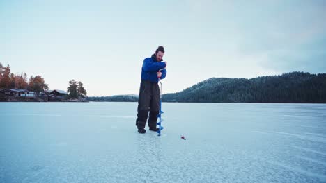Mann-Bohren-Auf-Eis-Mit-Schneckenbohrer---Eisfischen-Am-Zugefrorenen-See-Im-Winter-In-Norwegen