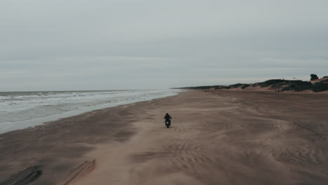 Aerial-View-of-Person-Wearing-All-Black-Riding-a-Motorcycle-On-The-Sand