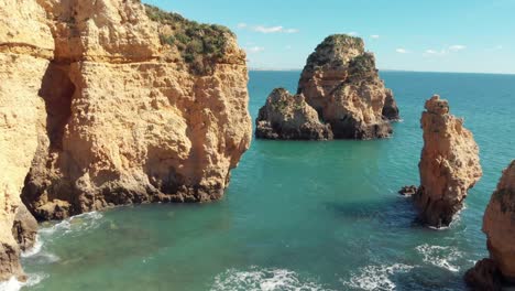 Sea-eroded-Rocky-sprouts-scattered-along-Algarve-shore,-in-Lagos,-Portugal---Aerial-low-angle-fly-over-shot