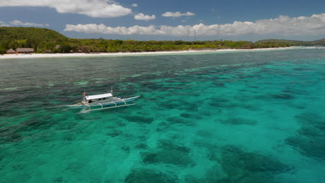 Aerial-showing-a-outrigger-boat-sailing-on-clear-blue-waters-in-Panglao-Island,-Bohol,-Philippines