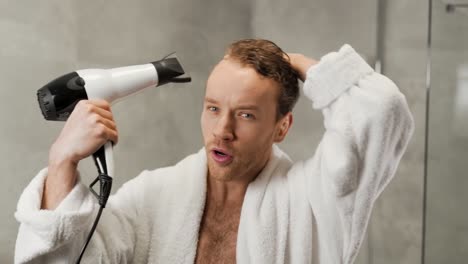 Handsome-man-in-a-white-bathrobe-dries-his-hair-with-a-hair-dryer