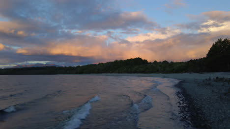 Dolly-Aus-Blick-Auf-Schnelle-Wellen,-Die-Nach-Einem-Wunderschönen-Sonnenuntergang-Am-Felsigen-Strand-Des-Sees-Te-Anau-In-Neuseeland-Zusammenbrechen