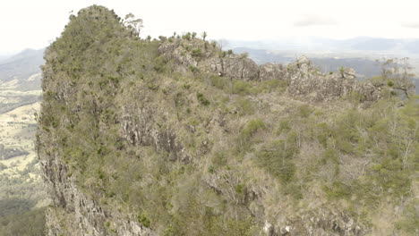 4K-drone-orbit-shot-of-hikers-walking-on-the-side-of-a-mountain-spine-cliff-at-Border-Ranges-National-Park,-New-South-Wales-Australia
