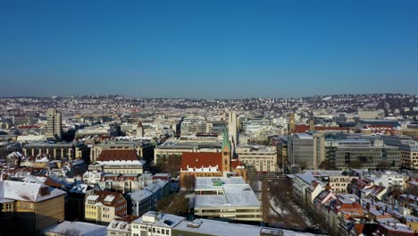 Aerial-flying-across-beautiful-city-center-with-red-tile-roofs,-streets-and-mounatins-covered-in-snow-during-winter-in-Leonhardsviertel-Stuttgart,-Germany