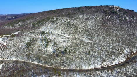 Aerial-drone-video-footage-of-a-snowy,-blue-sky-mountain-valley-road-highway-through-the-mountains-in-the-Appalachians-on-the-Shawangunk-ridge,-in-new-York-state