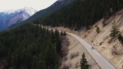 White-truck-drives-along-road-through-forest-landscape-in-British-Columbia,-Canada