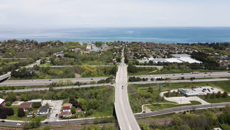 Aerial-pan-shot-showing-bridge-road-following-over-asphalt-highway-towards-Lake-Ontario-during-summer-day