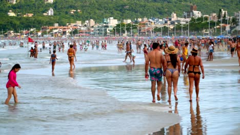 People-walking-in-wet-sand-by-the-seashore-enjoying-the-summer-day-in-Bombas-and-Bombinhas-beaches,-Brazil