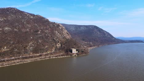 Aerial-drone-footage-approaching-breakneck-ridge-in-the-Appalachian-mountains-over-a-river-in-new-york's-hudson-valley-during-early-spring-at-the-hudson-river-with-blue-skies