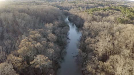 A-river-with-dead-trees-at-its-edges---aerial-view-with-tilt-up-to-reveal-a-wider-landscape