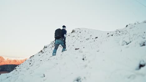 Young-man-hiking-uphill-on-a-snow-covered-mountain-in-Hoddevik,-Norway