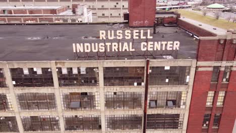 Logo-sing-of-aged-Russel-Industrial-Center-building-complex-in-Michigan,-aerial-side-fly-shot