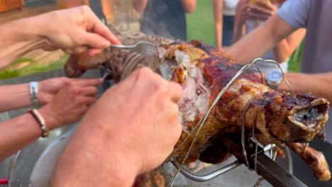 Men-hands-cutting-a-whole-lamb-with-forks-like-savages-on-a-spit-metal-stick-with-golden-crispy-skin,-lamb-bbq-grill,-4K-shot