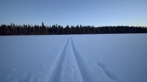 Trail-of-a-sled-leading-toward-a-forest-over-a-frozen-lake