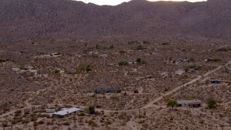 Aerial-over-dirt-road-and-small-houses-in-desert-of-Joshua-Tree,-California-with-a-car-on-a-dirt-road