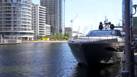 Large-luxury-boat-is-docked-on-the-side-of-the-canal-in-Canary-Wharf,-London-during-a-sunny-summer-morning-with-the-modern-apartment-buildings-in-the-background
