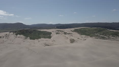 Aerial-view-of-the-sand-dunes-in-Llani,-Chile-with-patches-of-green-on-it-and-the-mountains-in-the-background