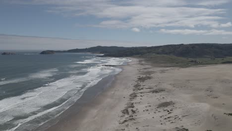 Push-iun-shot-of-the-coast-in-the-sand-Dunes-of-Llani,-Chile-taken-during-the-day-with-a-forest-in-the-back-ground