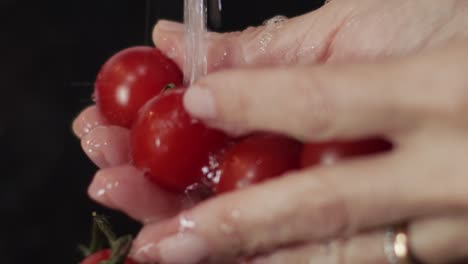 hands-rinsing-a-bunch-of-ripe-red-cherry-tomatoes-under-the-water-tap---close-up-shot