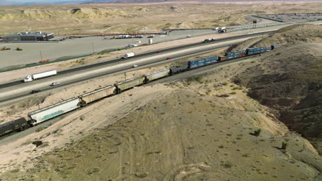 Automóviles-Y-Camiones-Semirremolque-Circulando-Por-El-Largo-Tren-De-Carga-Con-Petroleros-Y-Vagones-En-Nevada,-Ee.uu.