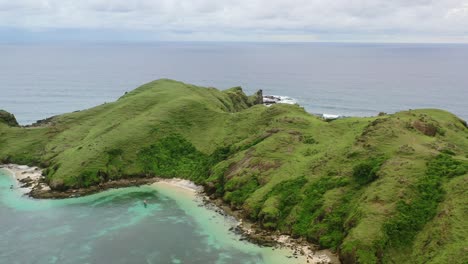 green-meadow-hills-on-overcast-day-at-Bukit-Merese-Lombok-surrounded-by-tropical-ocean,-aerial