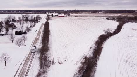 Farmer-haul-white-horse-trailer-on-winter-road-in-rural-area-of-Michigan,-aerial-shot