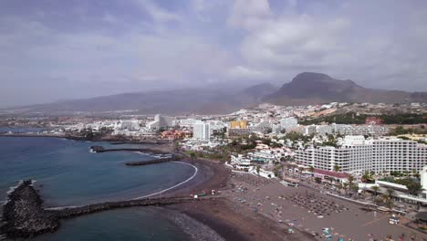 Vista-Aérea-De-Pedestal-De-Una-Playa-De-Arena-Negra-Cerca-De-La-Ciudad-Turística-De-Tenerife