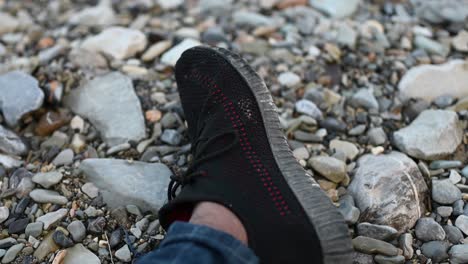 View-Of-Left-leg-wearing-black-trainer-resting-on-pebbles