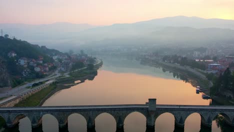 Person-walking-over-bridge-in-Visegrad,-top-down-aerial-sunset-mist