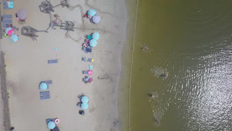 4k-drone-view-from-above-of-people-bathing-on-a-beach-with-turquoise-green-water