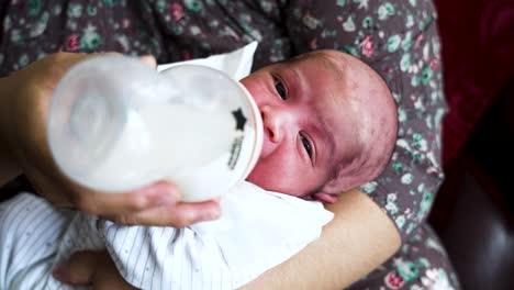 Entzückende-Nahaufnahme-Eines-Neugeborenen-Babys,-Das-In-Den-Armen-Seiner-Mutter-Liegt-Und-Sich-Von-Einer-Flasche-Muttermilch-Ernährt
