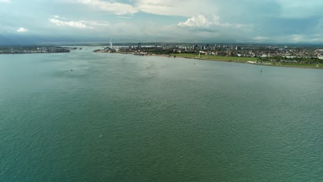 Flying-Above-Portsmouth-Harbour-With-Distant-View-Of-Spinnaker-Tower-In-Portsmouth,-UK