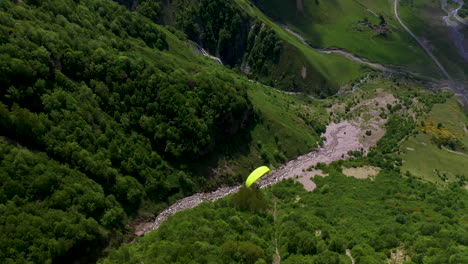 Downward-angle-rotating-drone-shot-of-paraglider-in-a-mountain-valley-in-Gudauri-Georgia,-the-Caucasus-mountains