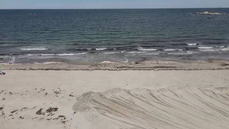 Track-Of-Heavy-Equipment-Wheel-On-Sandy-Beach-In-Cohasset,-Massachusetts-With-Atlantic-Ocean-Waves-In-Background