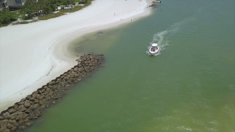 A-drone-shot-of-a-small-fishing-boat-passing-a-wall-of-rocks-in-Marco-Island,-Florida
