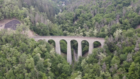 Stone-train-viaduct-over-a-mountain-valley-forests-in-Czechia,aerial