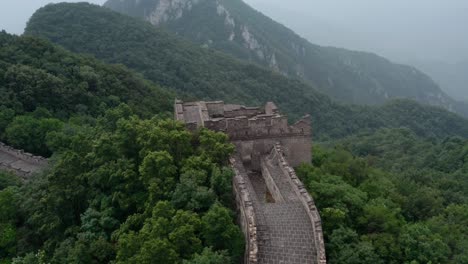Fly-over-deteriorated-lookout-tower-of-Great-Wall-of-China-on-top-of-green-mountain-ridge-on-a-cloudy-day