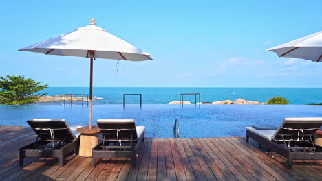 Infinity-Pool-Lounge-with-Deck-chairs-and-White-Umbrella-on-the-Rocky-Island-in-Bali-on-sunny-day