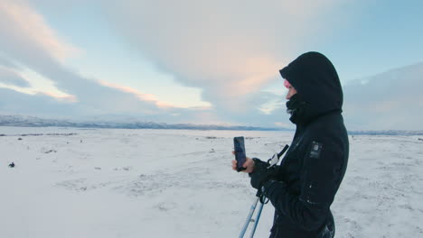 Female-cross-country-skier-filming-and-takes-photos-of-her-friend-with-her-mobile-phone-on-a-mountain-in-the-northern-Sweden