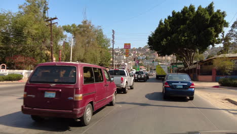 Driving-On-Busy-Street-In-Tijuana,-Mexico-On-A-Sunny-Day-With-Business-Establishments-Alongside