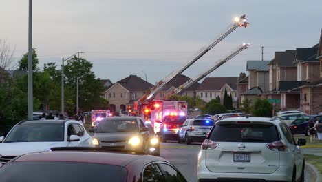 Traffic-crawling-slowly-through-residential-area-away-from-active-fire-perimeter-with-firefighters-working-on-aerial-ladders-of-various-fire-trucks,-Brampton-Canada