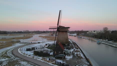 Dutch-Windmill-next-to-river-with-pink-clouds-in-background-at-dawn