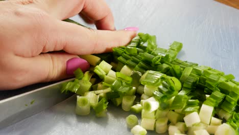 Female-cutting-fresh-spring-onions-on-blue-plastic-board,-close-up-view