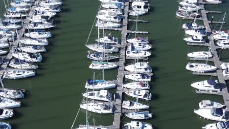 Flying-above-luxury-yachts-and-sailboats-reflections-on-sunny-Conwy-marina-birdseye-aerial-view-truck-left