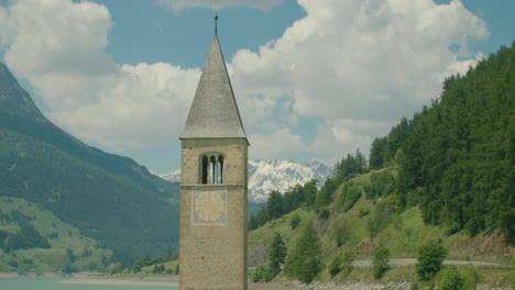 Mittlerer-Schuss,-Malerischer-Blick-Auf-Den-Kirchturm-Von-Altgraun-Am-Reschensee-In-Italien,-Bergkette-Im-Hintergrund