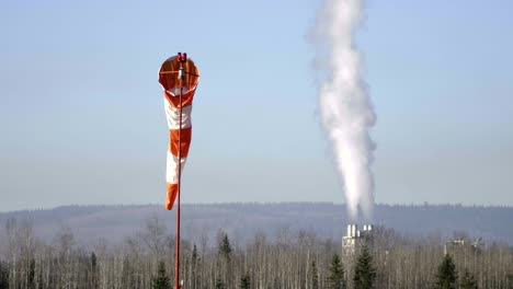 Windsock-At-Quesnel-Airport-With-Smoke-Coming-Out-On-Industrial-Chimney-In-Background-At-Quesnel,-British-Columbia,-Canada