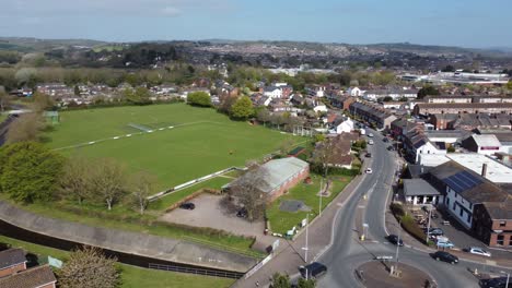 Aerial-drone-shot-panning-over-rural-football-pitch-and-housing-estate,-England