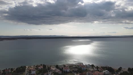 Sun-shimmering-over-Adriatic-in-Vrsi-Mulo-with-small-boat-passing-and-aerial-view-of-red-rooftops,-Croatia-in-Spring