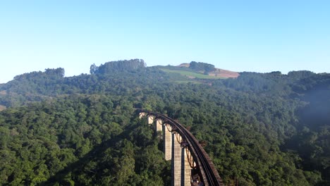 Aerial-view-of-high-railroad-bridge-track-accross-a-valley-into-a-hill-with-native-forest-under-the-morning-mist